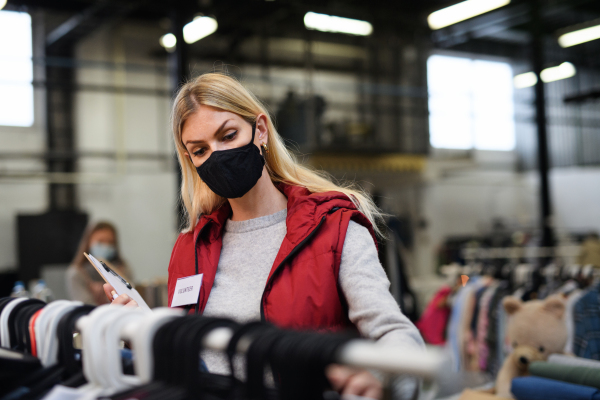 Woman volunteer working with clothes in community charity donations center, coronavirus concept.