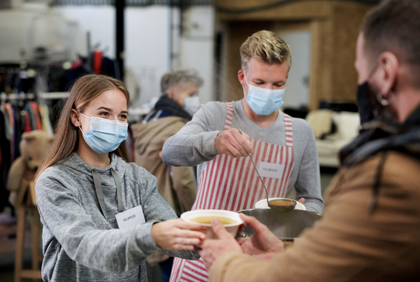 Volunteers serving hot soup for ill and homeless in community charity donation center, food bank and coronavirus concept.