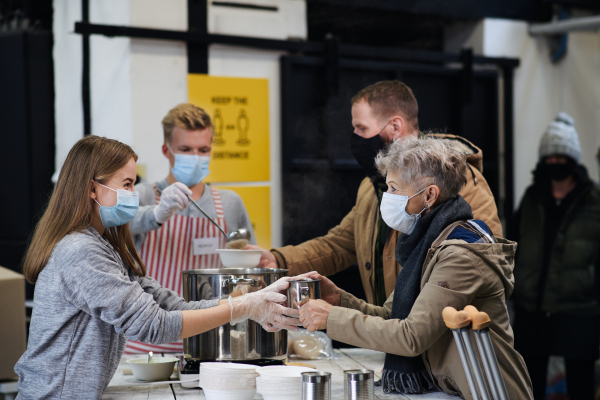 Volunteers serving hot soup for ill and homeless in community charity donation center, food bank and coronavirus concept.