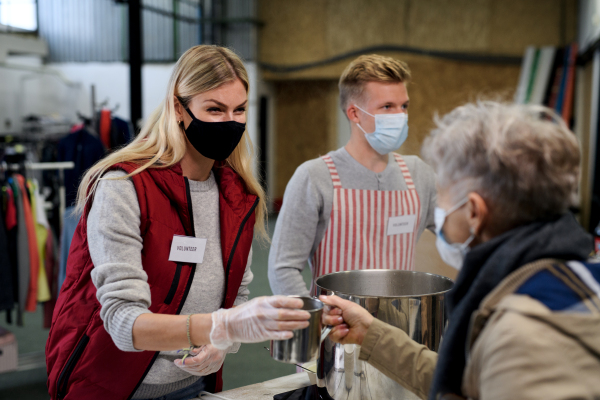 Volunteers serving hot soup for ill and homeless in community charity donation center, food bank and coronavirus concept.