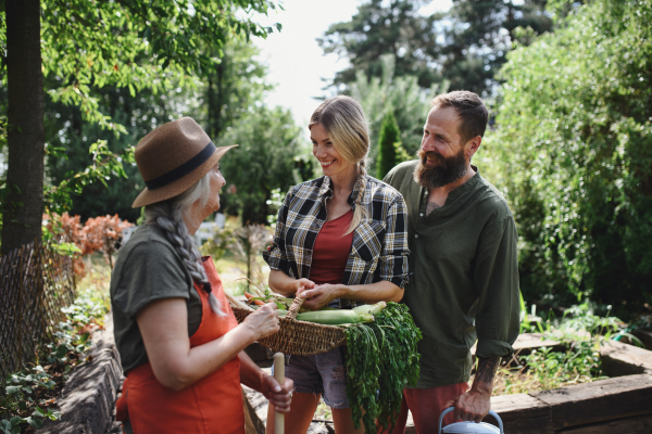 Happy farmers carrying a basket with homegrown vegetables outdoors at community farm.