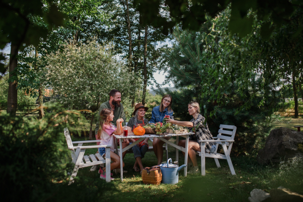 A happy family of farmers sitting by the table and looking at their harvest outdoors at community farm.