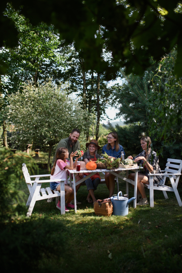 A happy family of farmers sitting by the table and looking at their harvest outdoors at community farm.