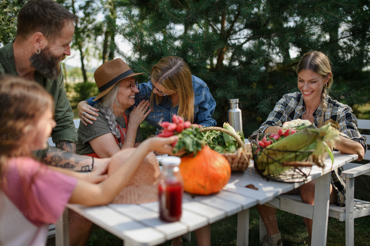 A happy farmer family sitting at table and looking at their harvest outdoors in garden.