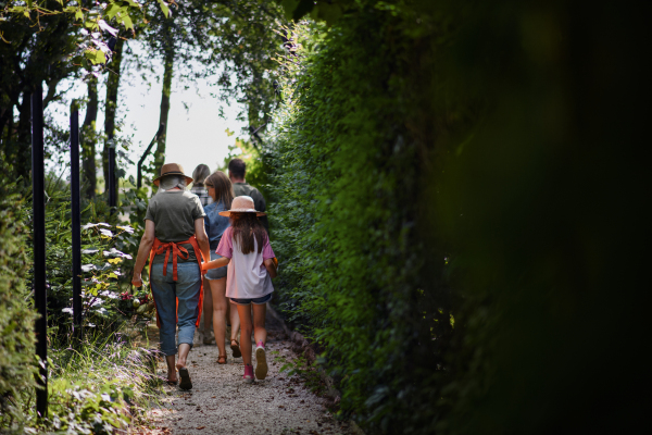 A rear view of happy young and old farmers or gardeners carrying their harvest outdoors at community farm.