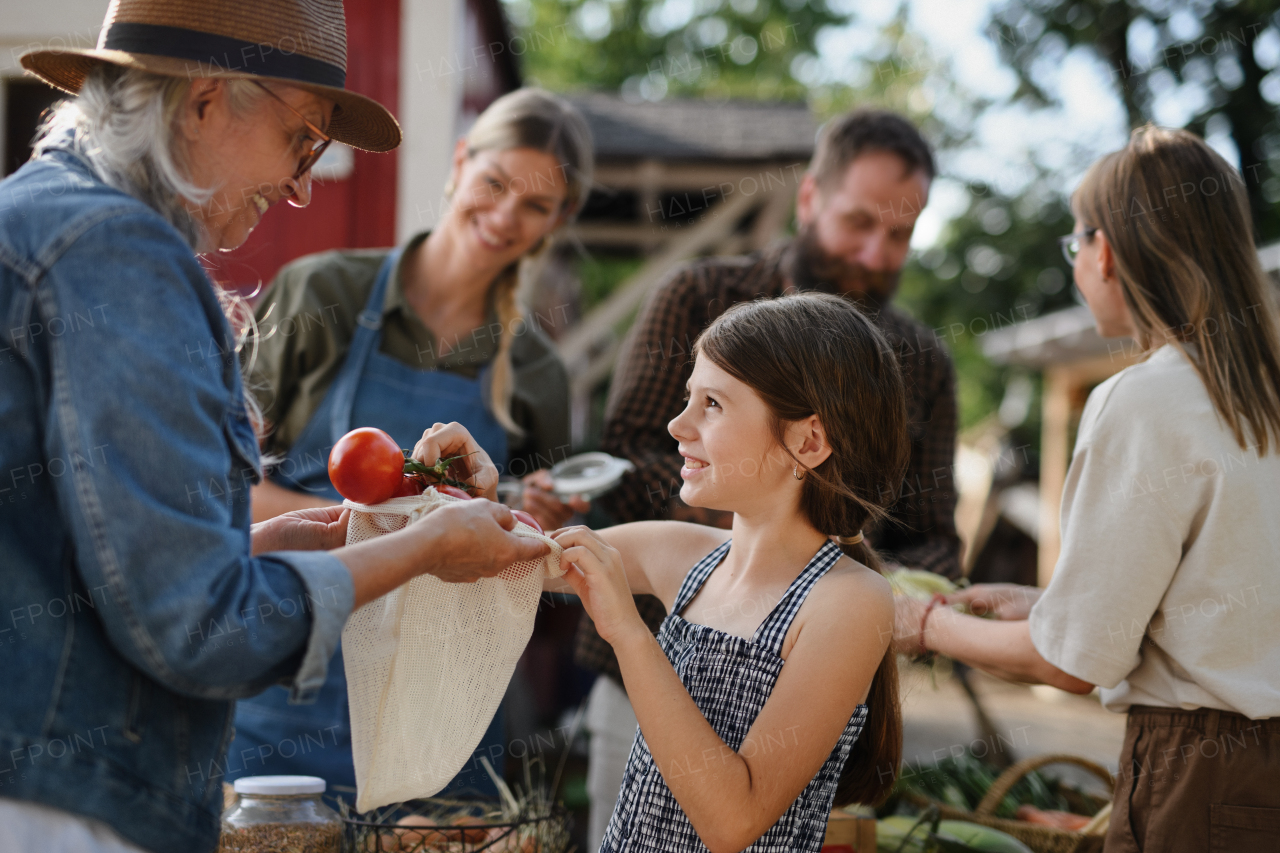 A little girl buying organic vegetables outdoors at community farmers market.