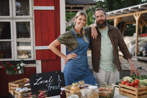 Mature couple farmers selling homegrown products at a community farmers market, looking at camera.