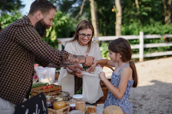 A happy little girl with mother buying vegetables outdoors at local family farmers market.