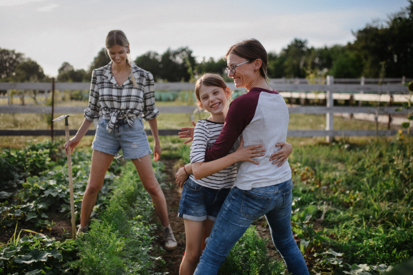 A happy little girl with mother hugging outdoors at community farm.