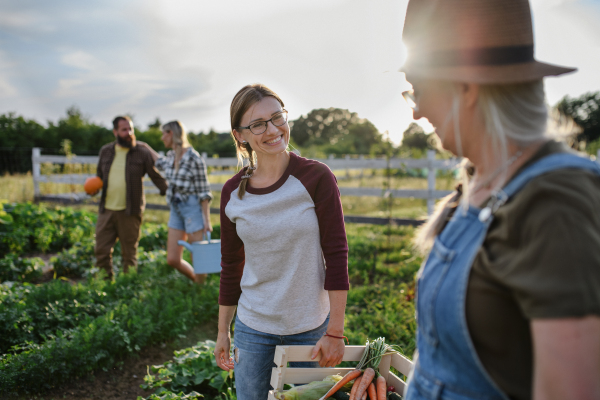 Happy mid adult female farmer hugging her senior peer holding basket with homegrown vegetables outdoors at community farm.