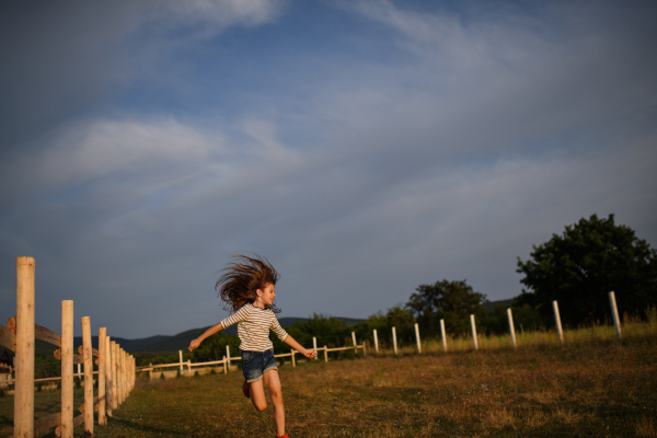 A happy little girl having fun and running outdoors in farm