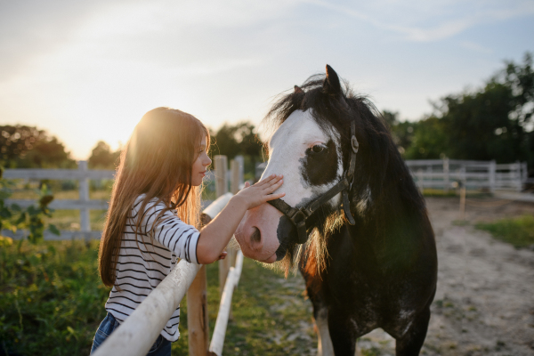 A little girl hugging horse outdoors at community farm.