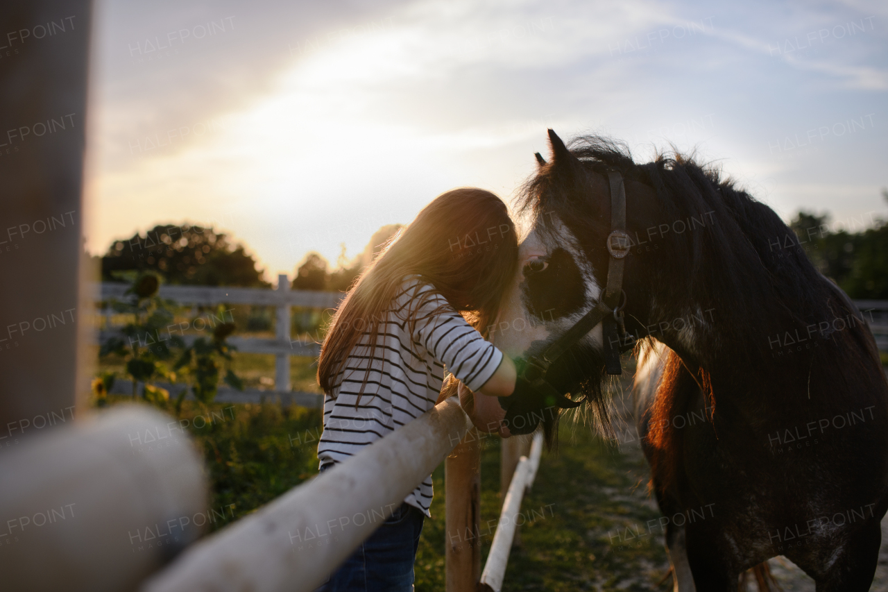 A little girl hugging horse outdoors at community farm.