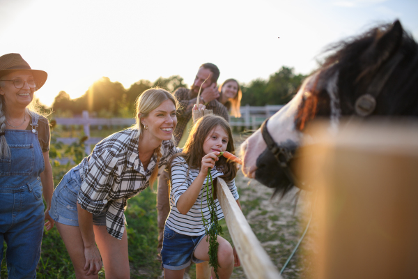 A little girl with mother feeding horse outdoors at community farm.