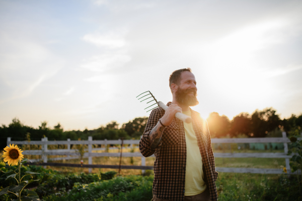 A happy mature farmer man with garden tool outdoors in field.