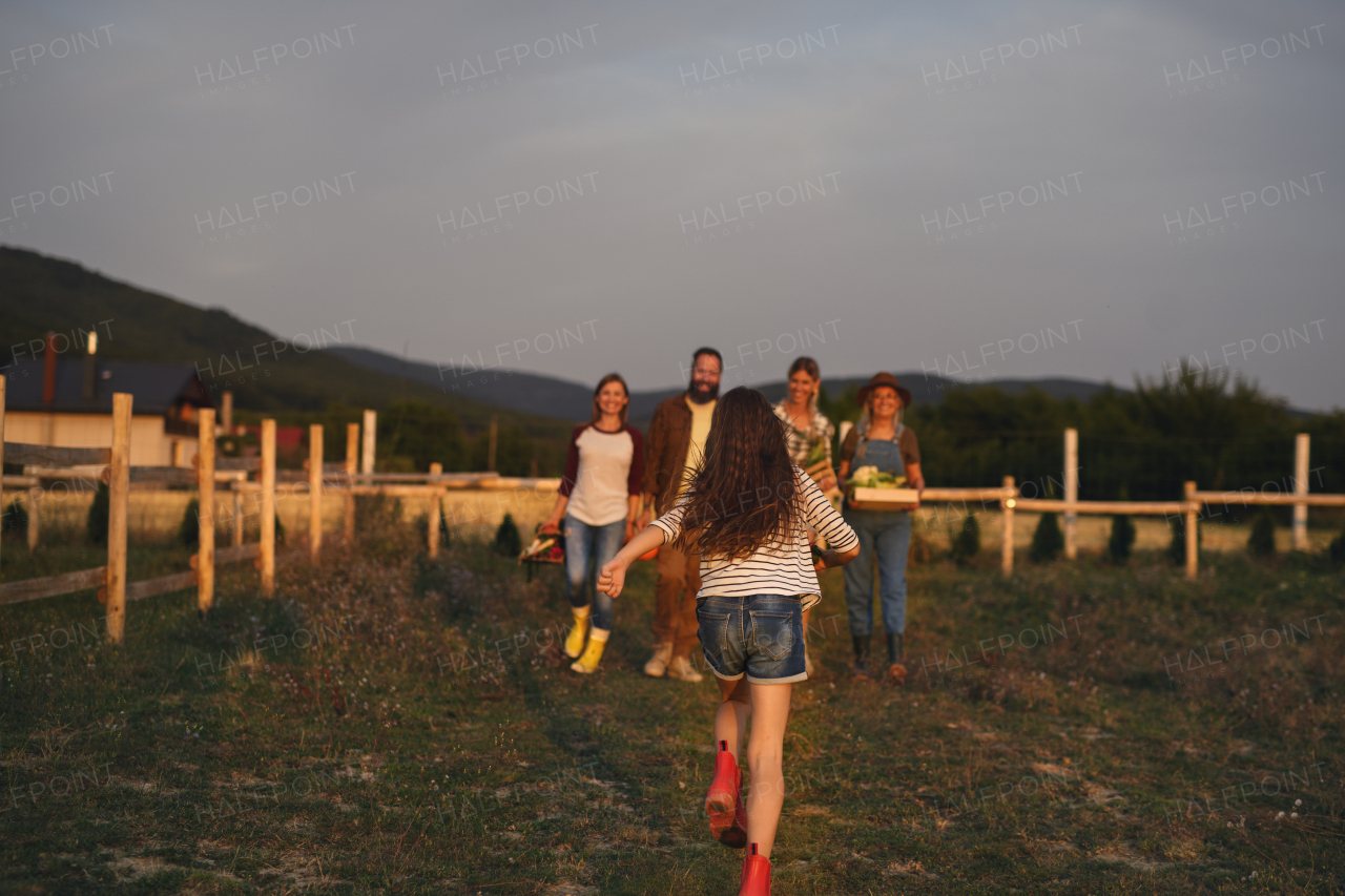 A rear view of little girl running to her family outdoors at community farm.