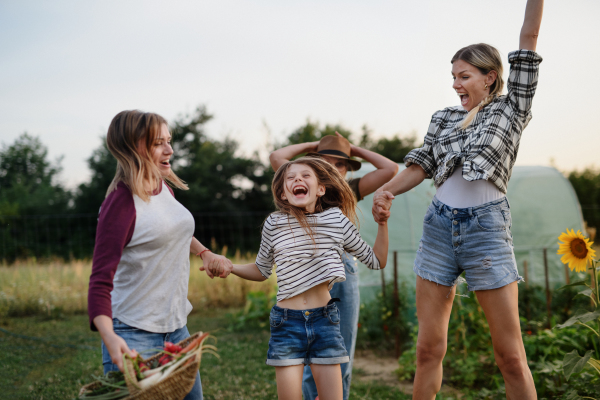 A happy little girl with mother and aunt jumping outdoors at community farm.