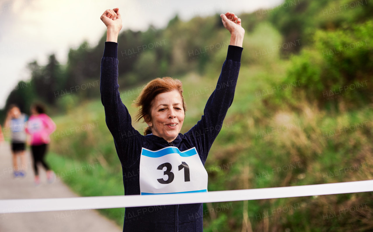 A senior woman runner crossing finish line in a race competition in nature.