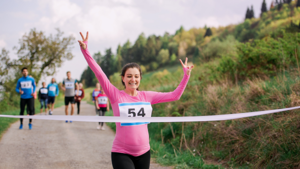 A young pregnant woman runner crossing finish line in a race competition in nature.