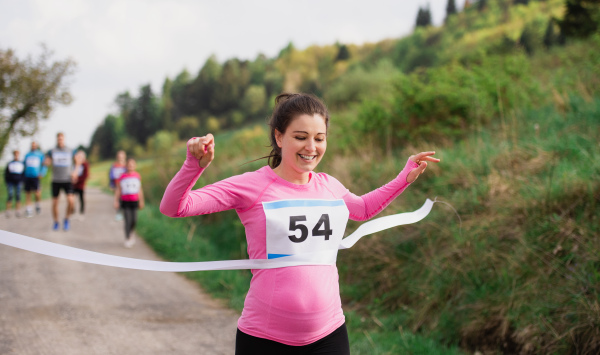 A young pregnant woman runner crossing finish line in a race competition in nature.