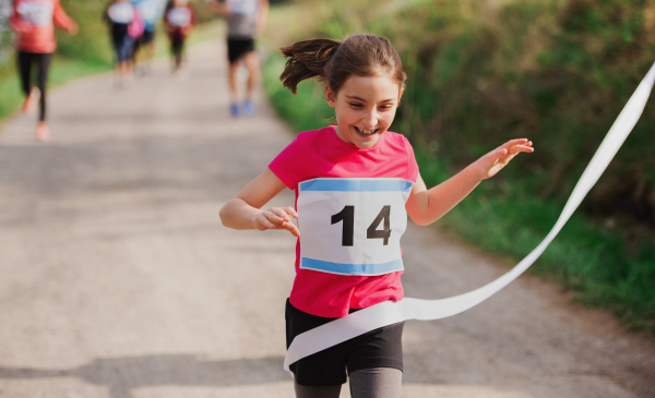 A small girl runner crossing finish line in a race competition in nature.