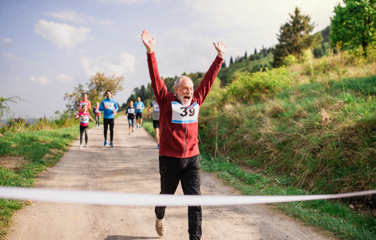 A senior man runner crossing finish line in a race competition in nature.