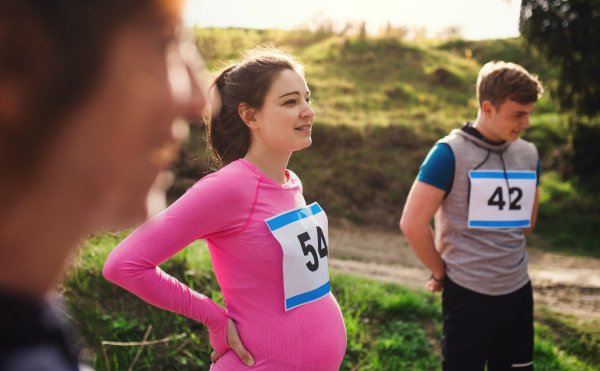 Fit and active pregant woman with friends doing exercise in nature, resting.