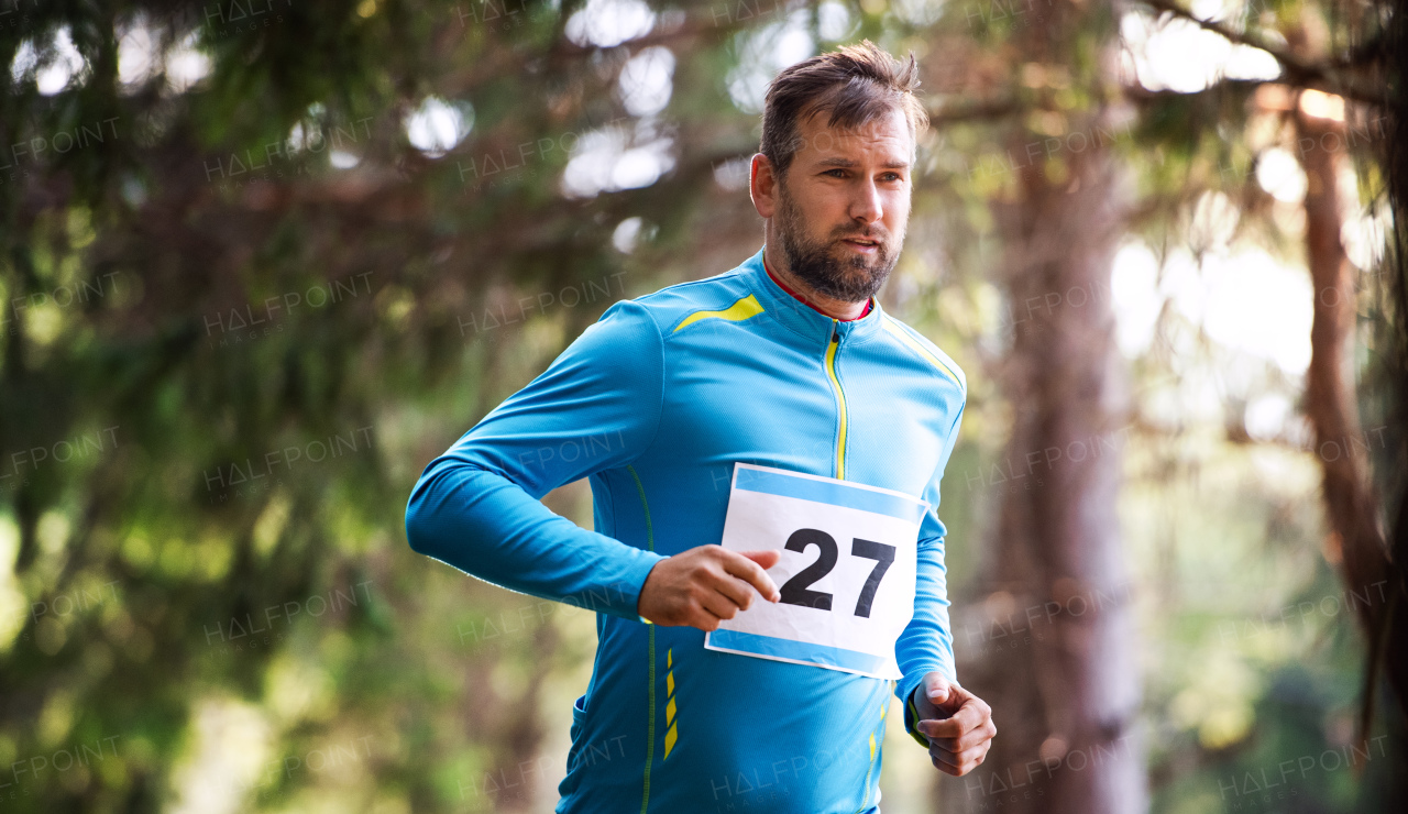 A front view of young man running a race competition in nature. Copy space.