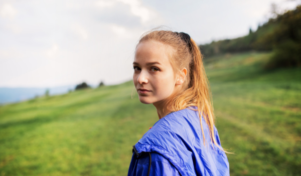 A portrait of young blond woman standing in nature, looking back.