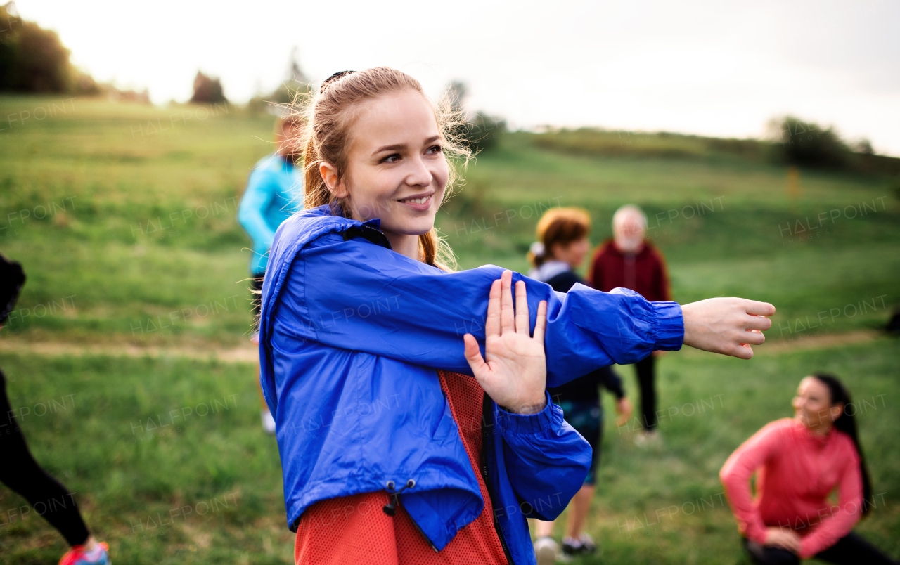 A large group of fit and active people doing exercise in nature, stretching.