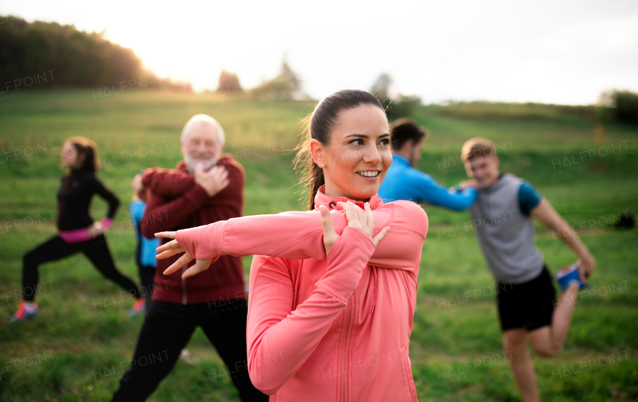 Front view of large group of fit and active people stretching after doing exercise in nature.