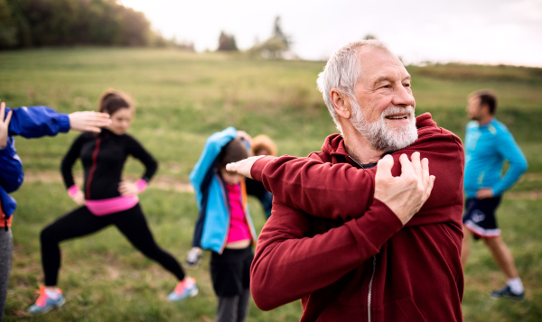 A large group of fit and active people doing exercise in nature, stretching.