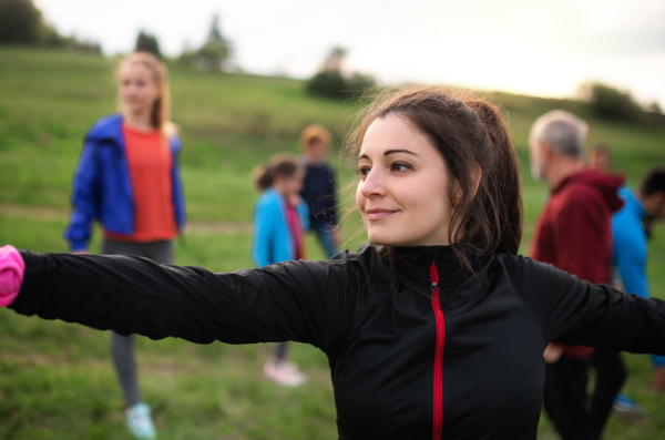 Front view of large group of fit and active people stretching after doing exercise in nature.