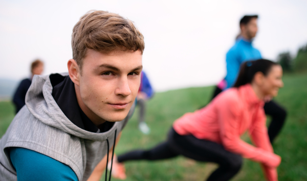 Front view of large group of fit and active people stretching after doing exercise in nature.