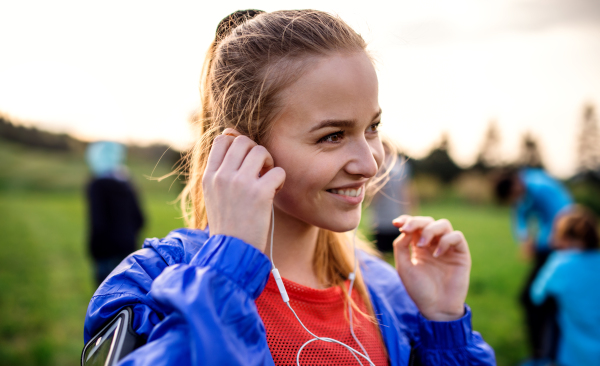 A portrait of young woman with earphones resting after doing exercise in nature.