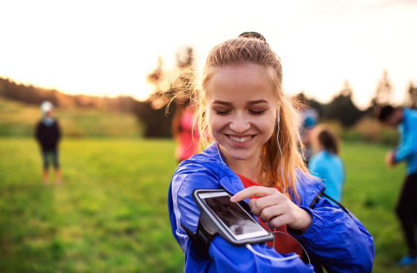 A portrait of young woman with smartphone and earphones resting after doing exercise in nature.