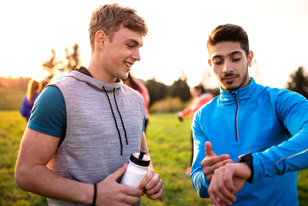 A portrait of young men with large group of people doing exercise in nature, resting.