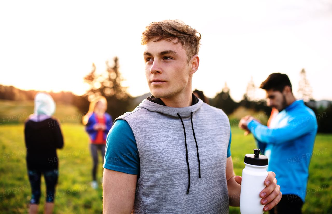 A portrait of young man with large group of people doing exercise in nature, resting.