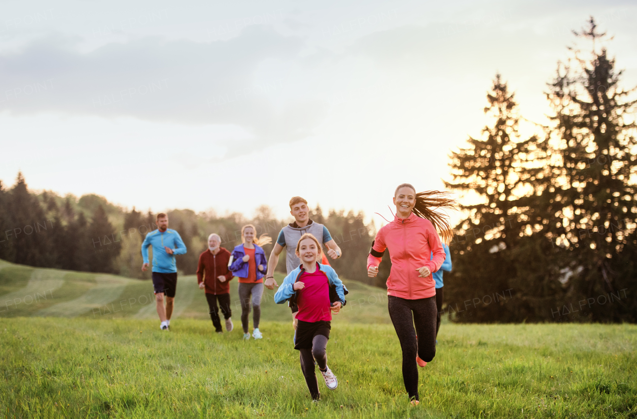 A large group of people cross country running in nature at sunset.