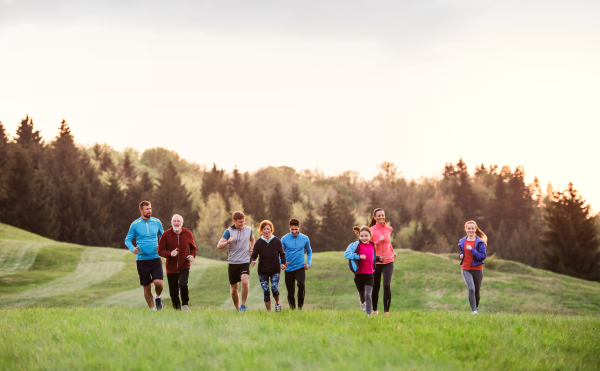 A large group of people cross country running in nature at sunset.