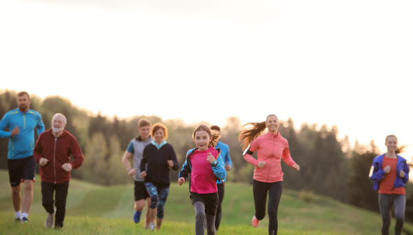 A large group of people cross country running in nature at sunset.