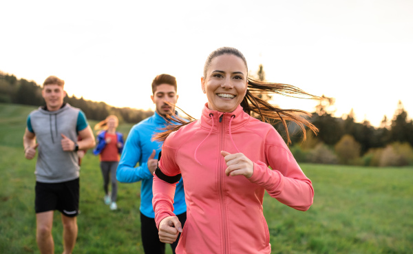 A large group of people cross country running in nature at sunset.