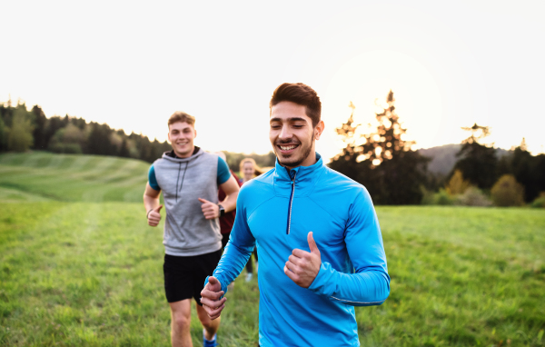 A large group of people cross country running in nature at sunset.