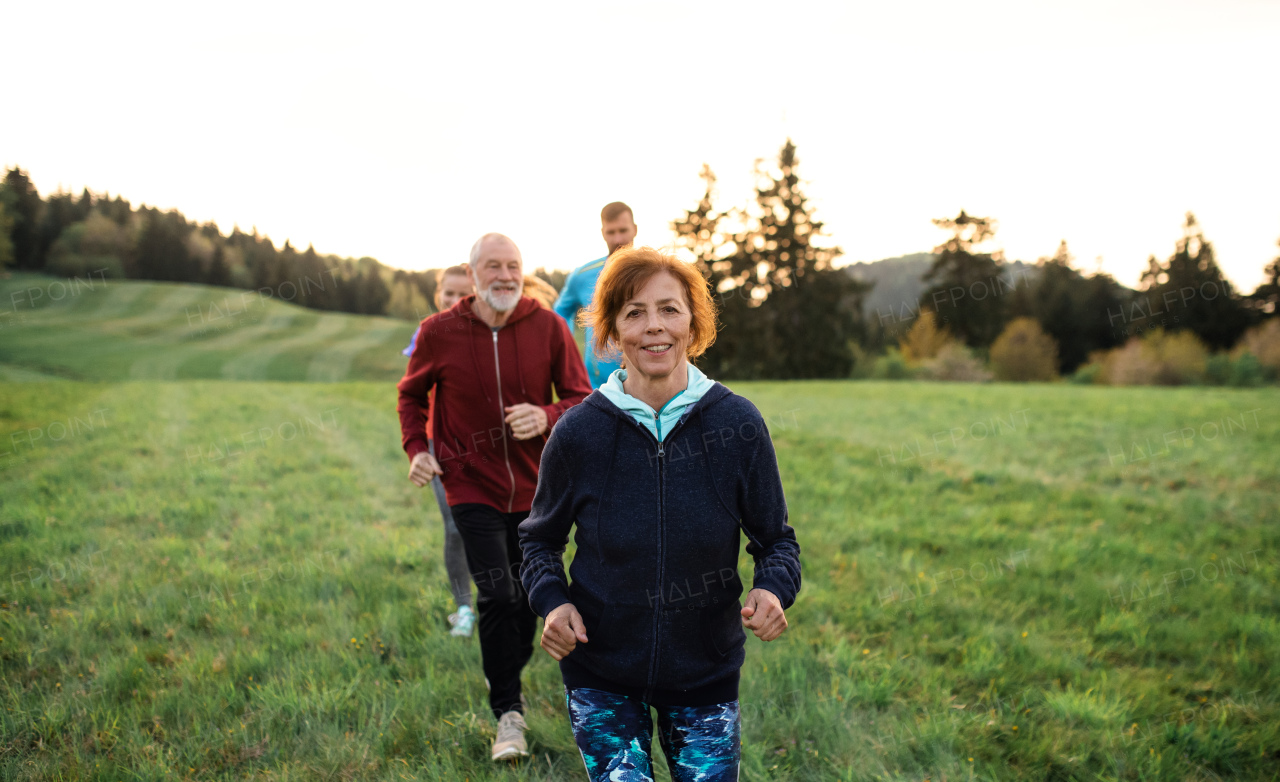 A large group of people cross country running in nature at sunset.