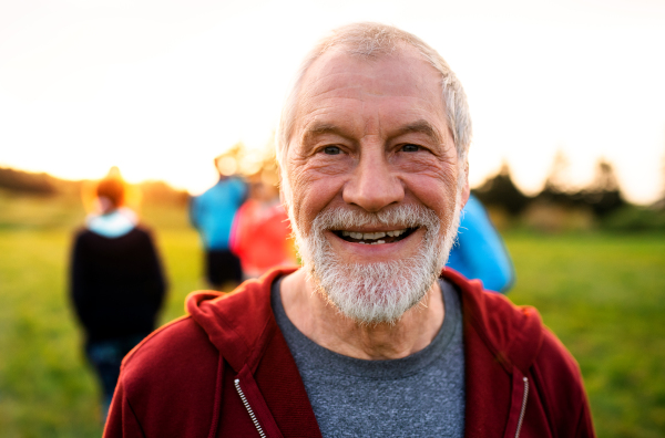 A portrait of senior man with large group of people doing exercise in nature, resting.