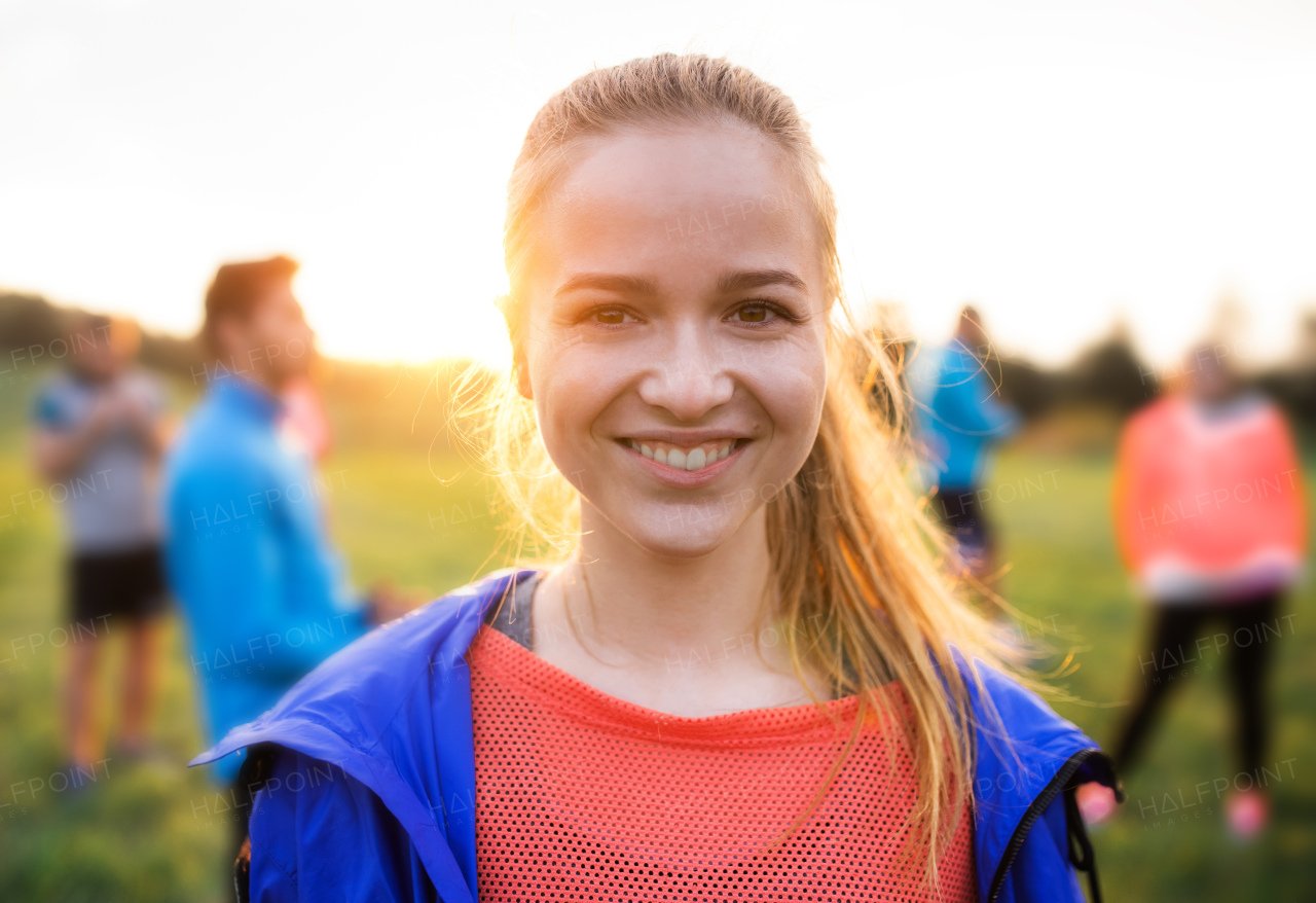 A portrait of young woman with large group of people doing exercise in nature, resting.