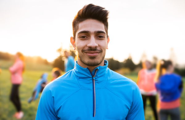 A portrait of young man with large group of people doing exercise in nature, resting.