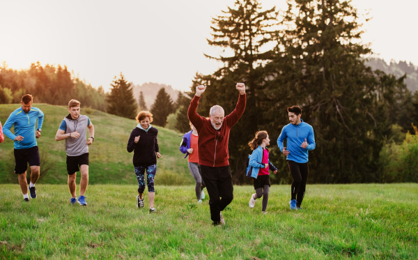 A large group of people cross country running in nature at sunset.