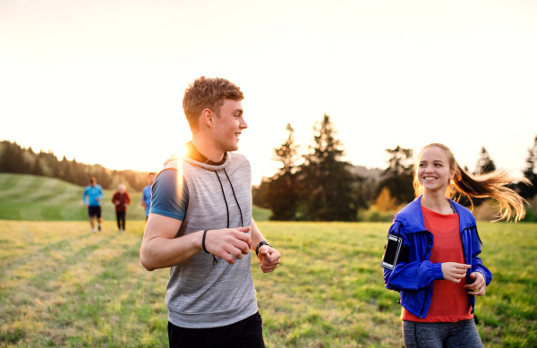 A large group of people cross country running in nature at sunset.