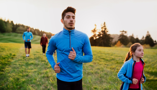 A large group of people cross country running in nature at sunset.